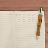 A cork pen with a green and white design resting on an opened notebook with handwritten text.