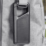 A portable black Bluetooth speaker attached to a grey bag with a strap. It has a textured surface and a prominent speaker grille.