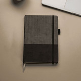 A5 Thermo notebook featuring recycled paper, with a textured grey and black cover, placed on a desk with a laptop.