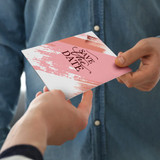 A5 greeting card in pink and white with a brushstroke design, held by one person and being handed to another.