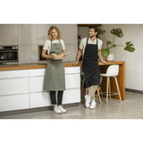 A green apron and a black apron worn by two people in a modern kitchen setting, featuring a logo on the aprons.