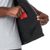 A person's hand reaching into a pocket inside a grey softshell vest, featuring a black interior. The vest has a logo.