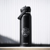 A drink bottle in matte black with a flip straw lid and a logo featuring a vanlife theme.