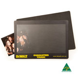 A natural rubber counter mat featuring a smooth black surface and a logo at the bottom, with a small photo included.