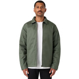 A man wearing a green service jacket over a white t-shirt, standing with a neutral expression. The jacket has a logo.