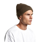 A ribbed olive green beanie is worn by a model, featuring a snug fit. The product has a logo.