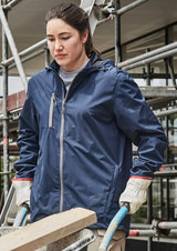 A woman in a navy blue packable rain jacket, wearing gloves, stands near scaffolding, holding a wooden beam.