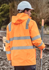 A person wearing an orange waterproof jacket with reflective stripes and a white hard hat, standing near railway tracks.