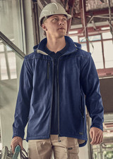A blue unisex softshell jacket features a hood, shown being worn by a person in a construction setting.