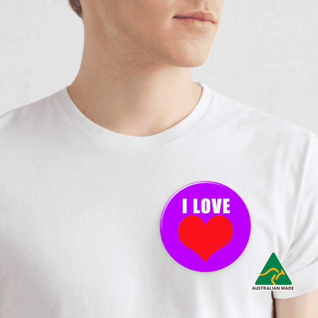 A purple button badge featuring a red heart design, attached to a white shirt on a plain background.