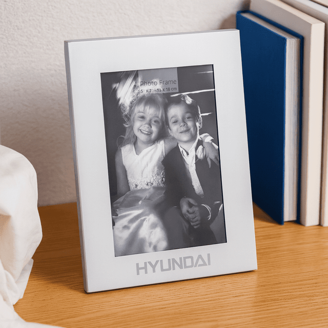 A silver aluminium photo frame displaying a black-and-white photo of two children. The frame features a logo at the bottom.