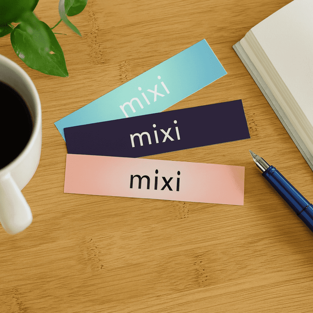 Gloss paper stickers in pastel blue, navy, and pink placed on a wooden surface beside a coffee cup and notebook.