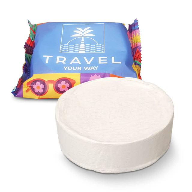 A round white compressed towel in front of colourful packaging featuring a logo.