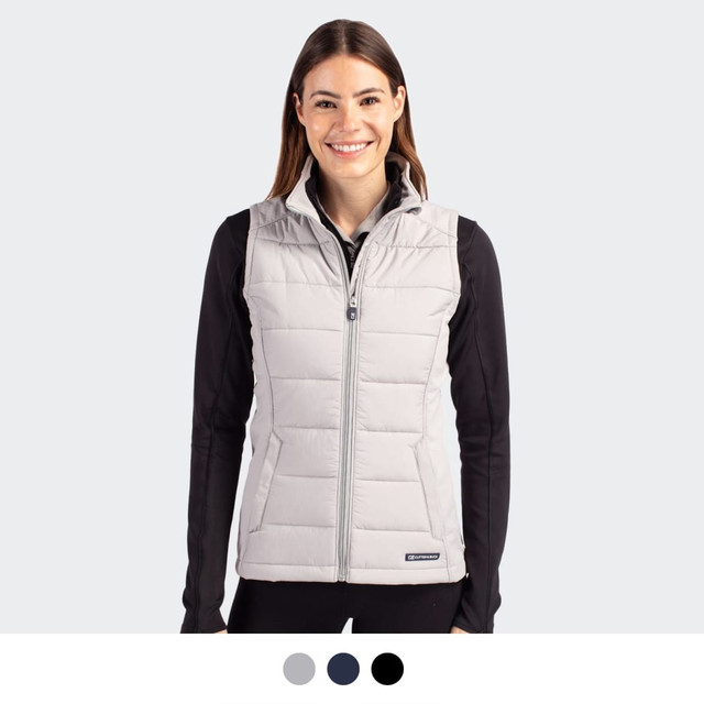 A woman wearing a light grey puffer vest with a zip front. The vest has a logo and is styled with a black top.