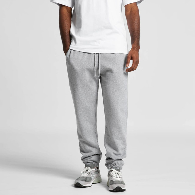 Grey track pants with elastic cuffs and a drawstring waist, worn with a white t-shirt and sneakers. Features a logo.