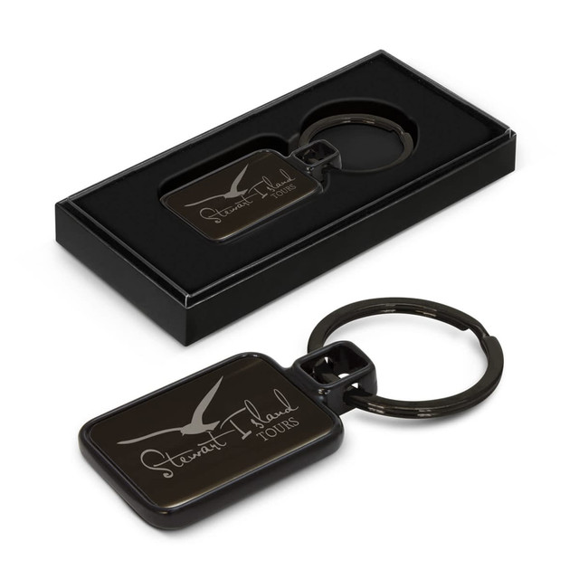 A black key ring with a rectangular tag in a box, featuring a branding logo on the tag.