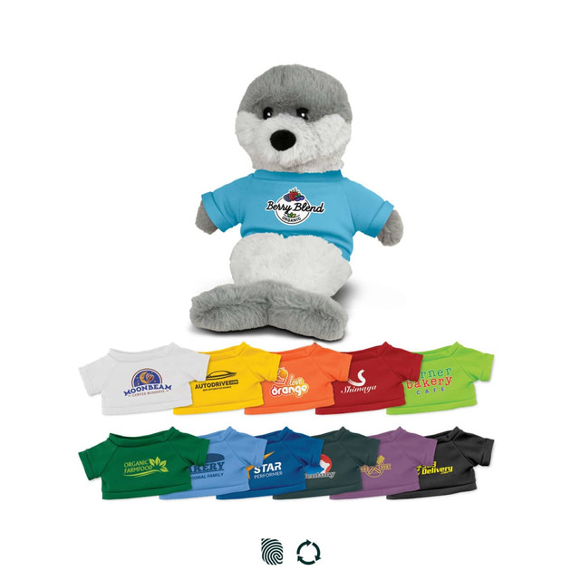 A plush seal toy with grey and white fur wearing a blue T-shirt. Various colourful miniature T-shirts are arranged below.