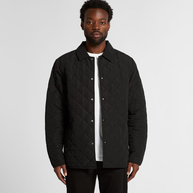 A man wearing a black quilted jacket with a button-up front and a collared neck. The jacket has a logo.