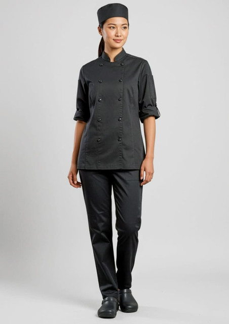 A woman wears a black chef's uniform, including a chef coat and flex pants, paired with a matching hat and footwear.