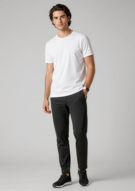 A model wearing black track pants paired with a white t-shirt and black sneakers, featuring a logo.