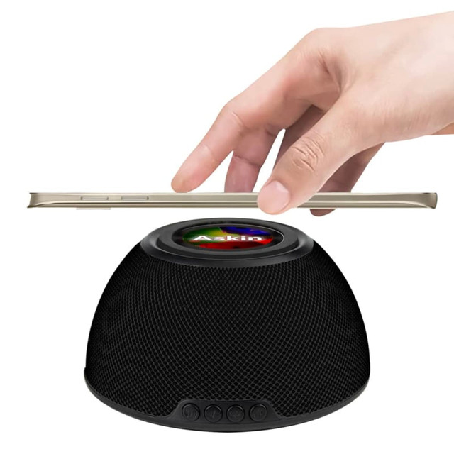 A black wireless charging speaker with a hand positioning a phone above it. It features a logo on the surface.