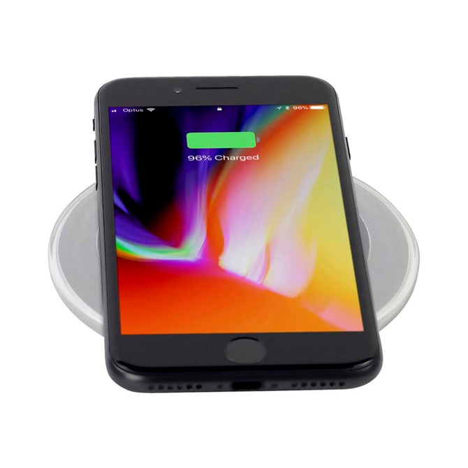 A black smartphone displaying a charged battery on a round, clear wireless charging pad. The pad has a subtle design.