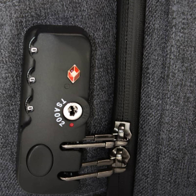 A close-up of a grey backpack zipper with a combination lock and branding on the side.