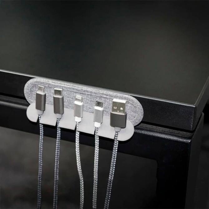 A cable organiser in grey holds multiple charging cables against a black surface. It features a fabric-like texture and a sleek design.