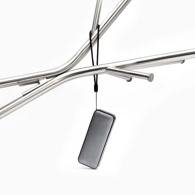 A compact black Bluetooth speaker hanging from a metal frame, featuring a sleek design and a strap.