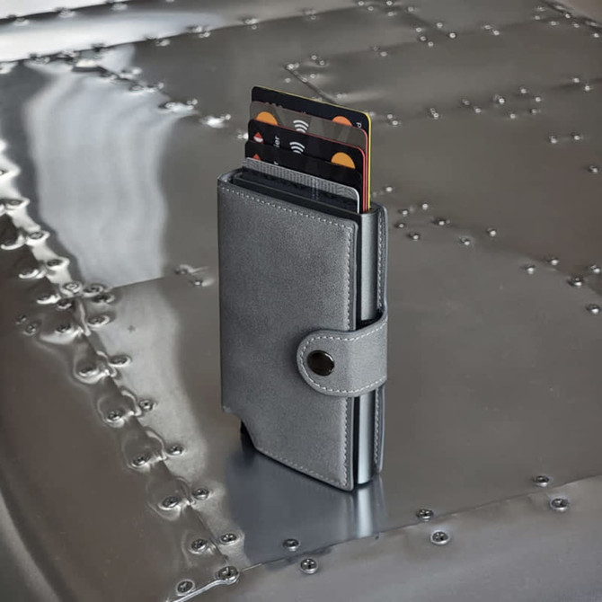 A grey vegan wallet stands upright on a metallic surface, displaying multiple cards partially visible from its opening.