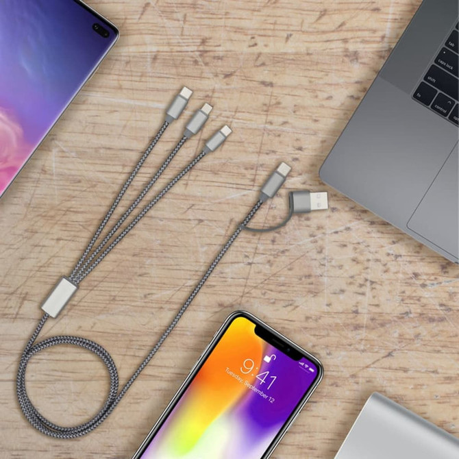 A charging cable with multiple connectors in grey, connected to a laptop and mobile devices on a wooden surface.