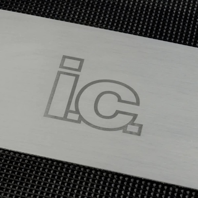 A stainless steel grilling spatula with engraved lettering on a textured black background.
