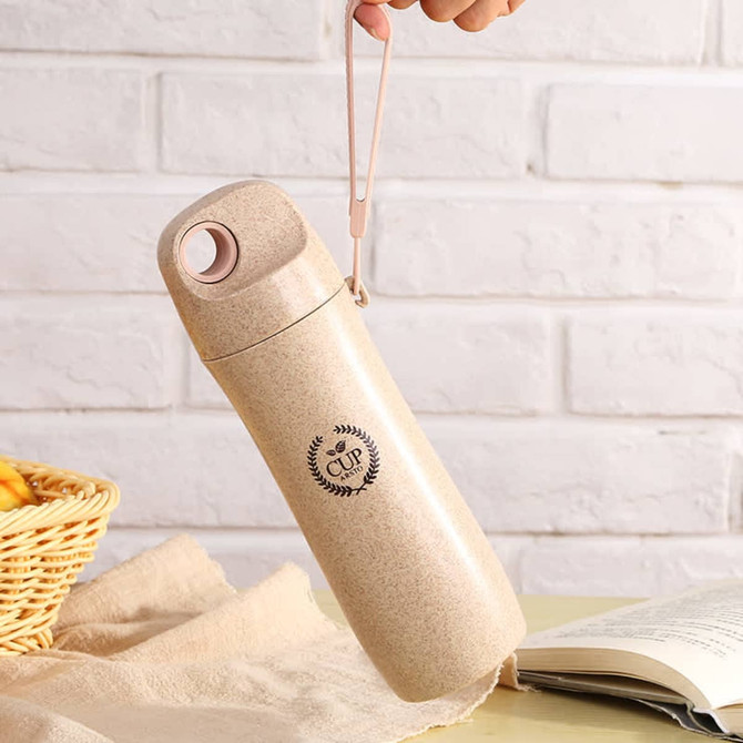 A drink bottle made from wheat straw in a beige colour, featuring a logo and a convenient carrying strap.