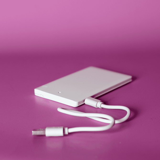 A white ultra slim power bank with a USB cable, set against a pink background.