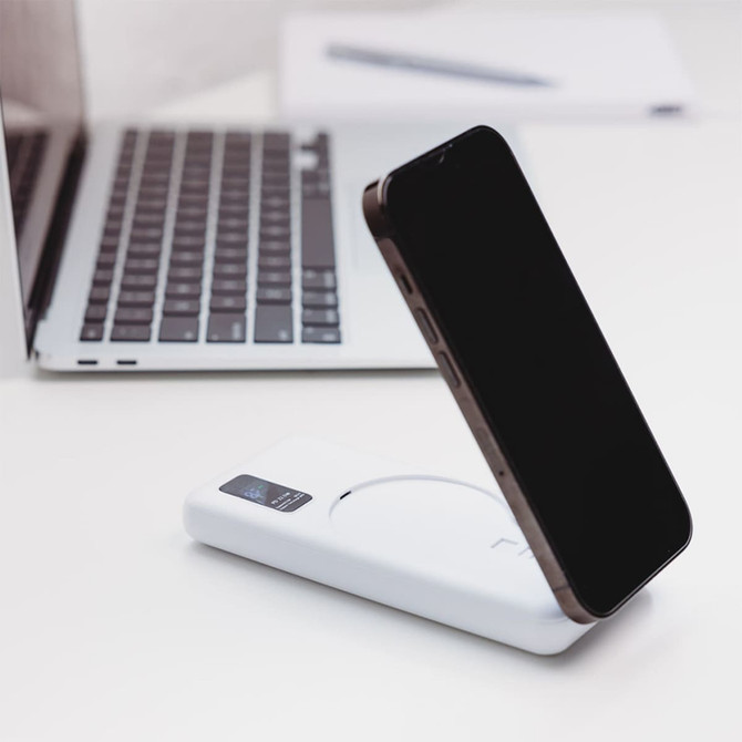 A white power bank with a wireless charging feature and a smartphone in the process of being charged.