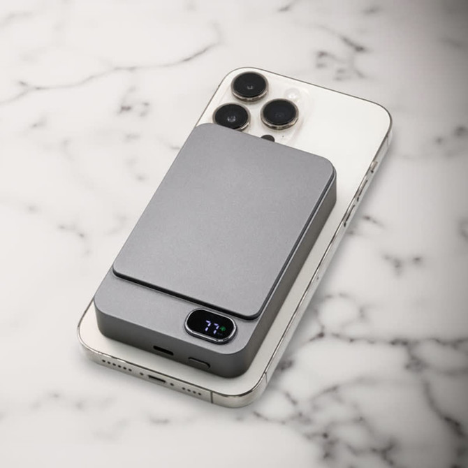 A grey magnetic wireless power bank rests on a smartphone, displaying a sleek and modern design against a marble background.