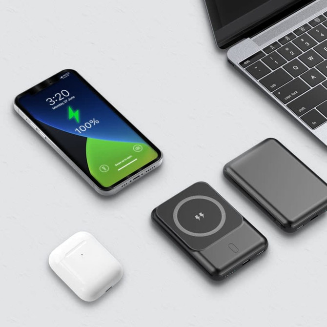 A power bank in black with a circular charging area, placed next to a smartphone and earbuds on a light surface.