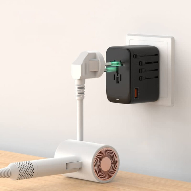 A black travel adaptor with multiple ports is plugged into a wall socket, connected to a white device.