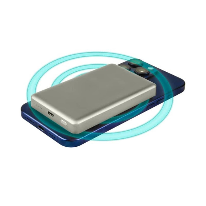 A silver 15W MagSafe wireless power bank placed on a blue smartphone, with a glowing ring indicating wireless charging.