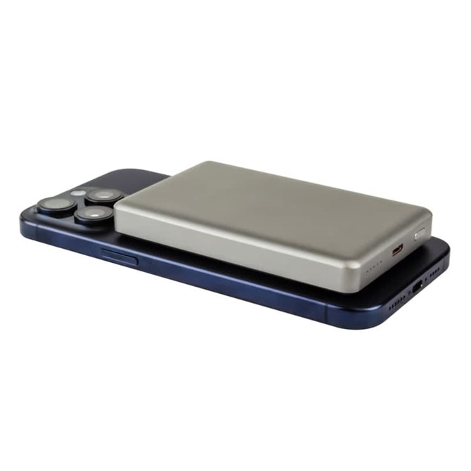 A silver MagSafe wireless power bank rests on a dark phone. The power bank has charging ports and a brand logo.
