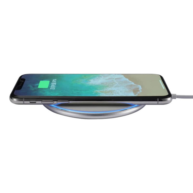 A silver wireless charger with a smartphone placed on top, showcasing a charging indicator.