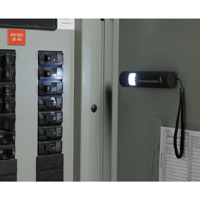 A black mini grip slim LED flashlight attached to a metal surface, illuminating electrical circuit breakers.
