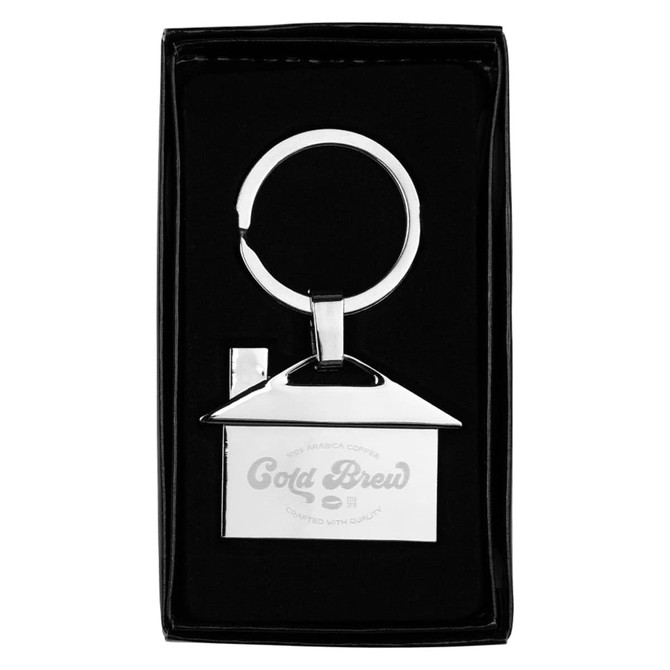 A house-shaped metal keyring in silver, displayed in a black box with a logo. It's sleek and stylish.
