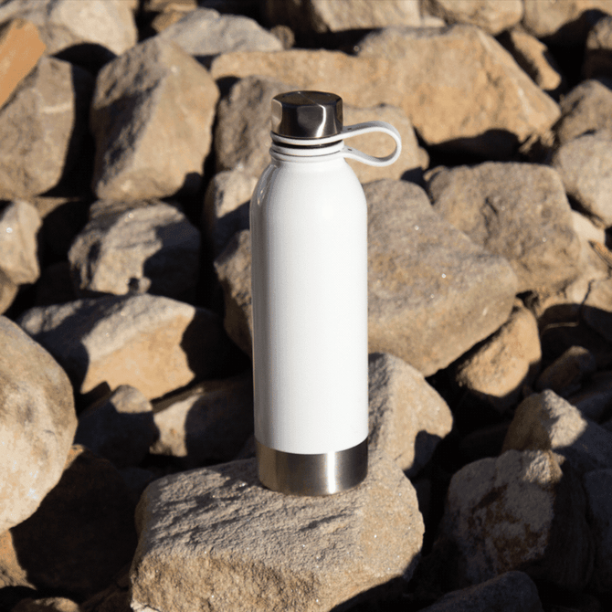 A drink bottle in white with a stainless steel base, featuring a loop cap, set on rocky terrain.