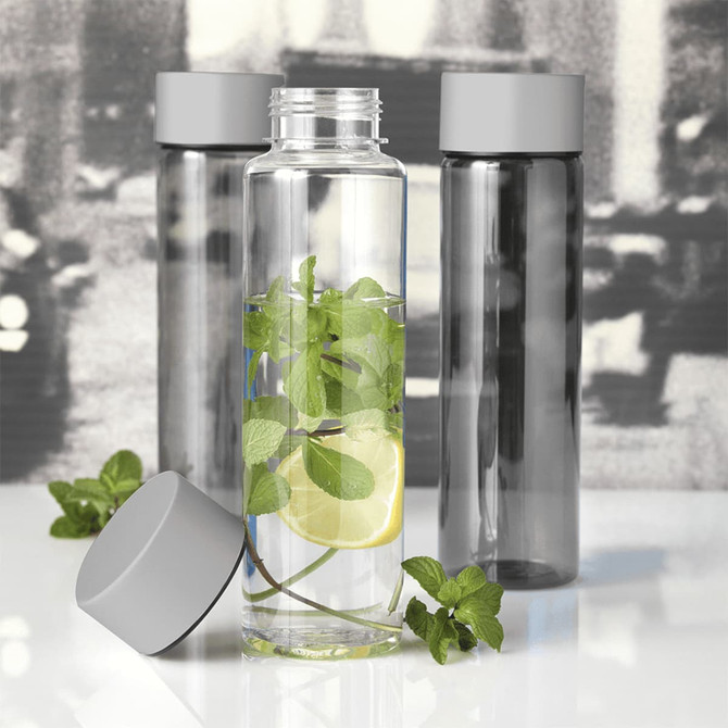 A drink bottle with a clear body, grey lid, and slices of lemon and fresh mint inside. Two additional opaque bottles are in the background.