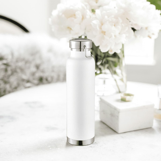 A drink bottle in white with a stainless steel base and cap, beside a flower arrangement on a table.