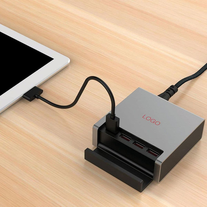 A USB smart charger in silver with multiple ports, connected to a tablet, resting on a wooden surface.