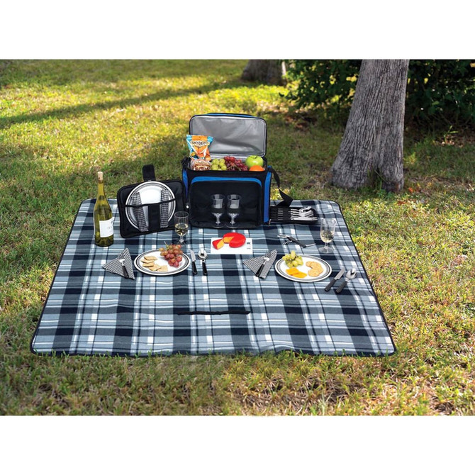 A picnic rug in shades of blue and grey, laid out with plates, glasses, cutlery, and a picnic basket on grass.