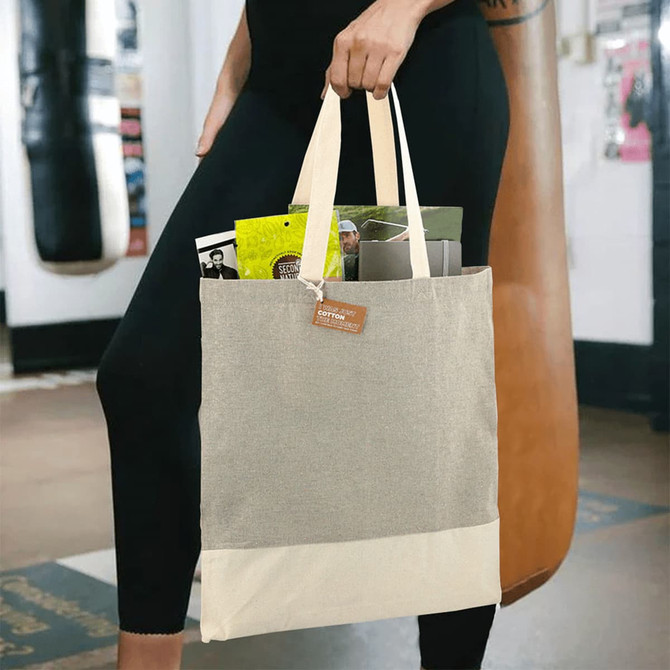 A beige and cream tote bag with a logo, held by a person, containing various items inside.