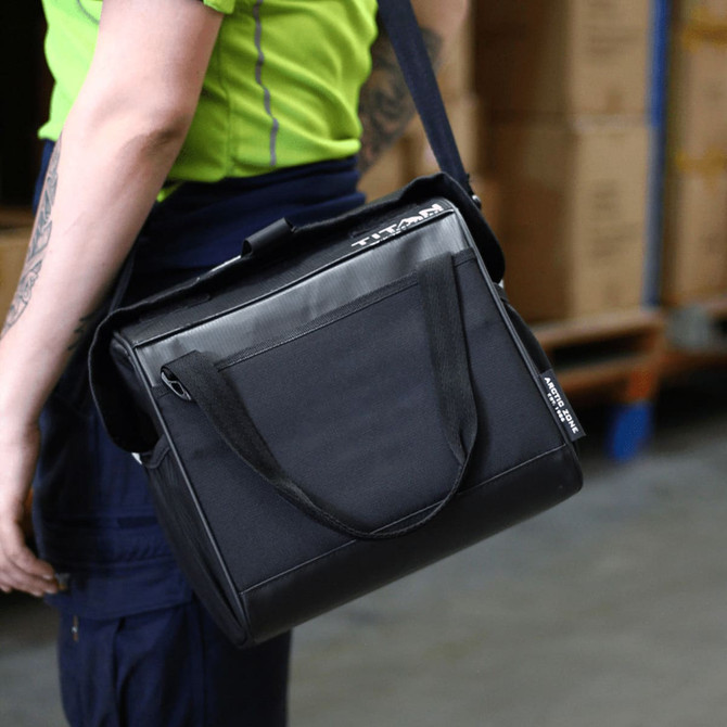A black lunch cooler with a shoulder strap, featuring a front pocket and branding, held by a person.